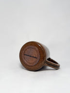 The bottom of a brown marbled stoneware mug that shows a smooth hand trimmed foot and 'elmstone studio' branding 